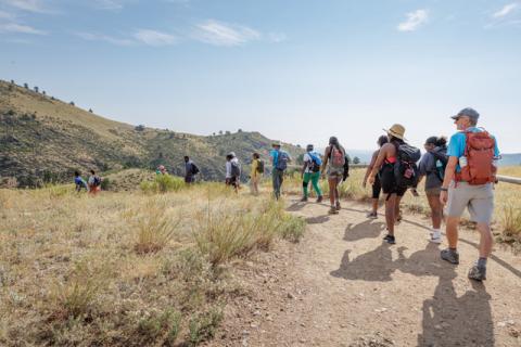 Vibe Tribe hikers walk a dirt trail at Devil's Backbone under a sunny sky.