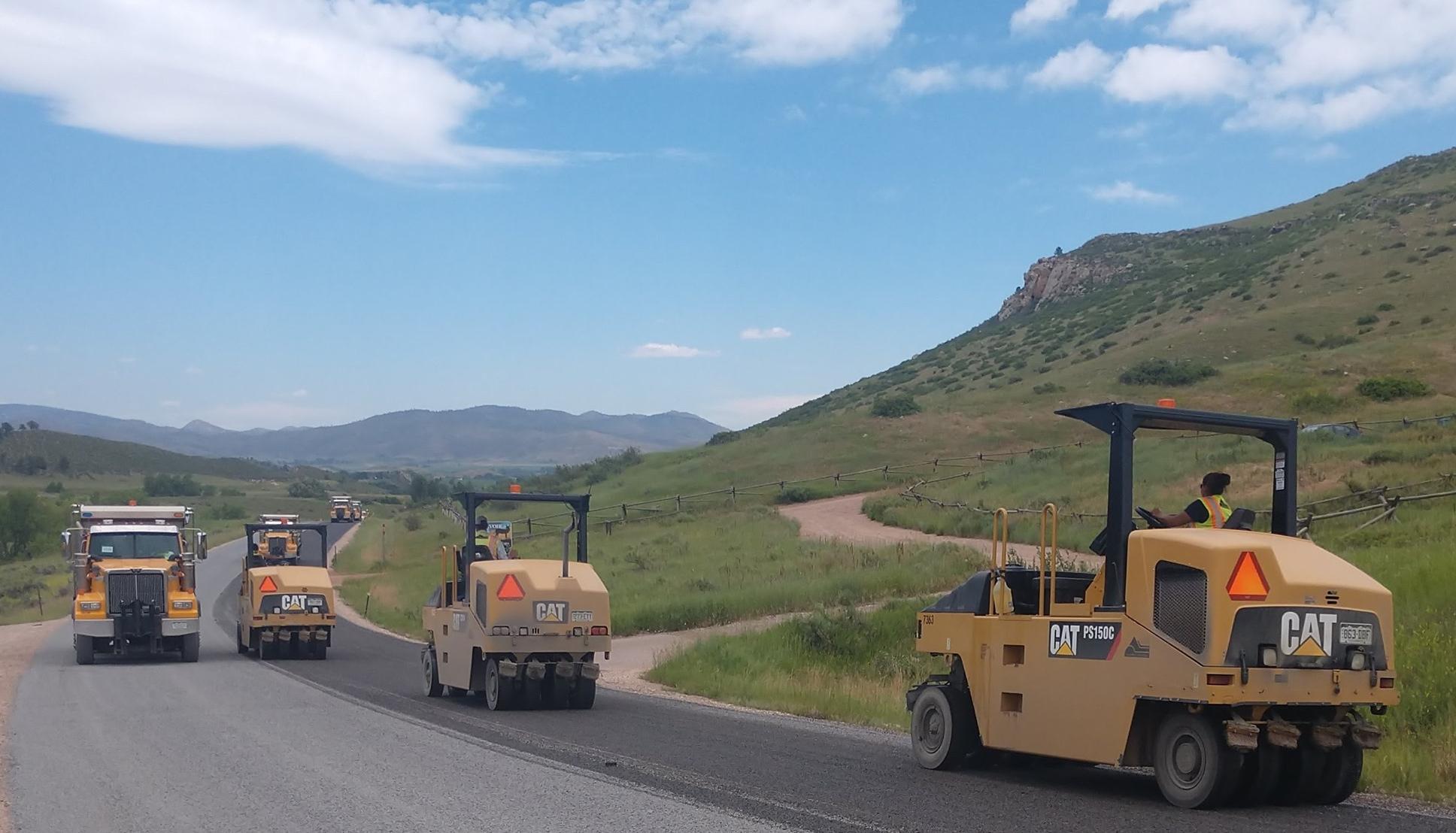 large road maintenance vehicles perform road work on a rural road in Larimer County.