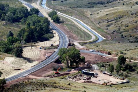 A road crossing an irrigation ditch lined with trees with erosion control on shoulders