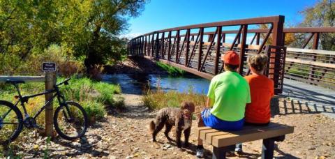 A family resting on a bench near a bridge on the Poudre River Trail