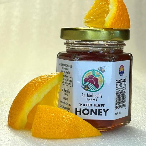 A jar of St. Michael's Farms Pure Raw Honey with orange slices around it.