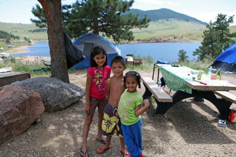 Three kids stand at a campground at Pinewood Reservoir