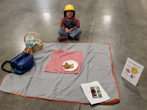 A Larimer County 4-H Member at Creative Cooks. His display is spread-out in front of him.  It is a  builder/construction themed picnic.