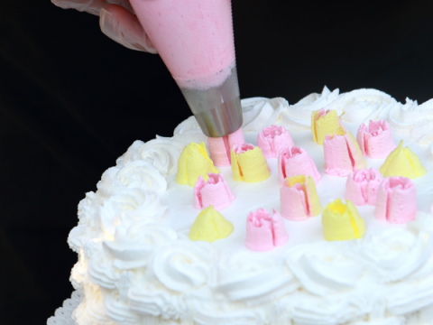 A cake that is being decorated with white, yellow, and pink frosting.