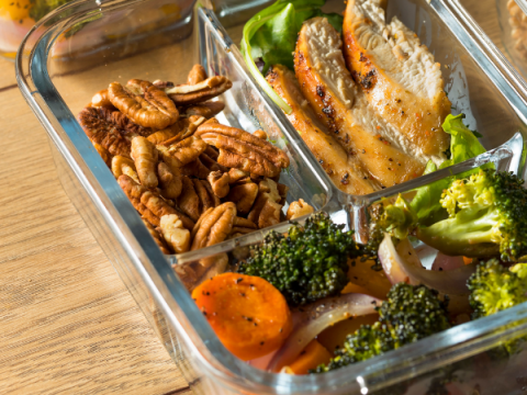 Pecans, a healthy salad, and grilled chicken in a meal prep container. 