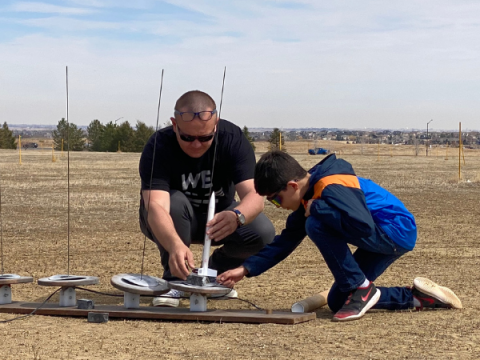 A 4-H leader helps a young man set up his model rocket preparing it to launch